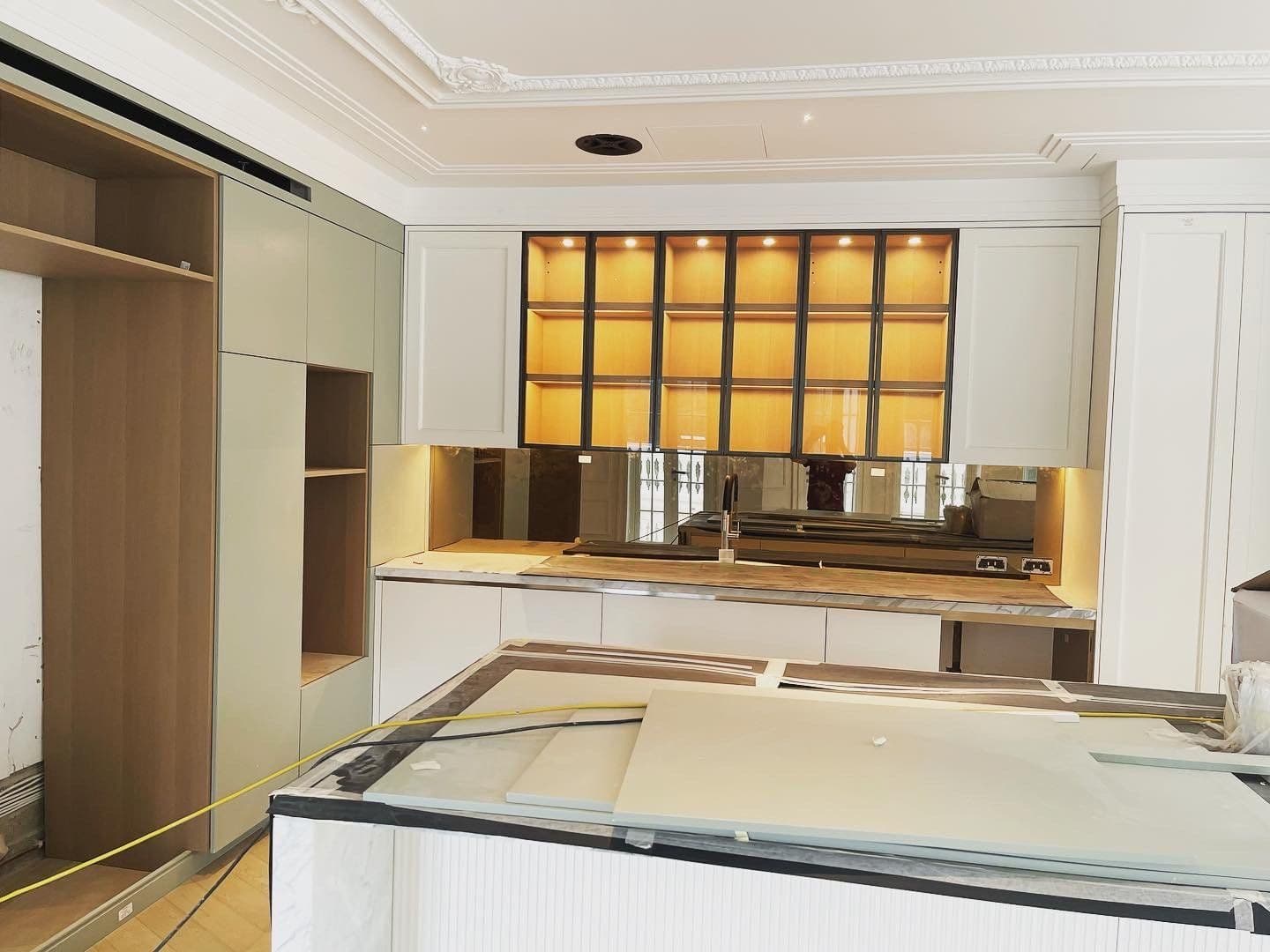Bespoke kitchen mid-installation with backlit display cabinetry and mirror splashback