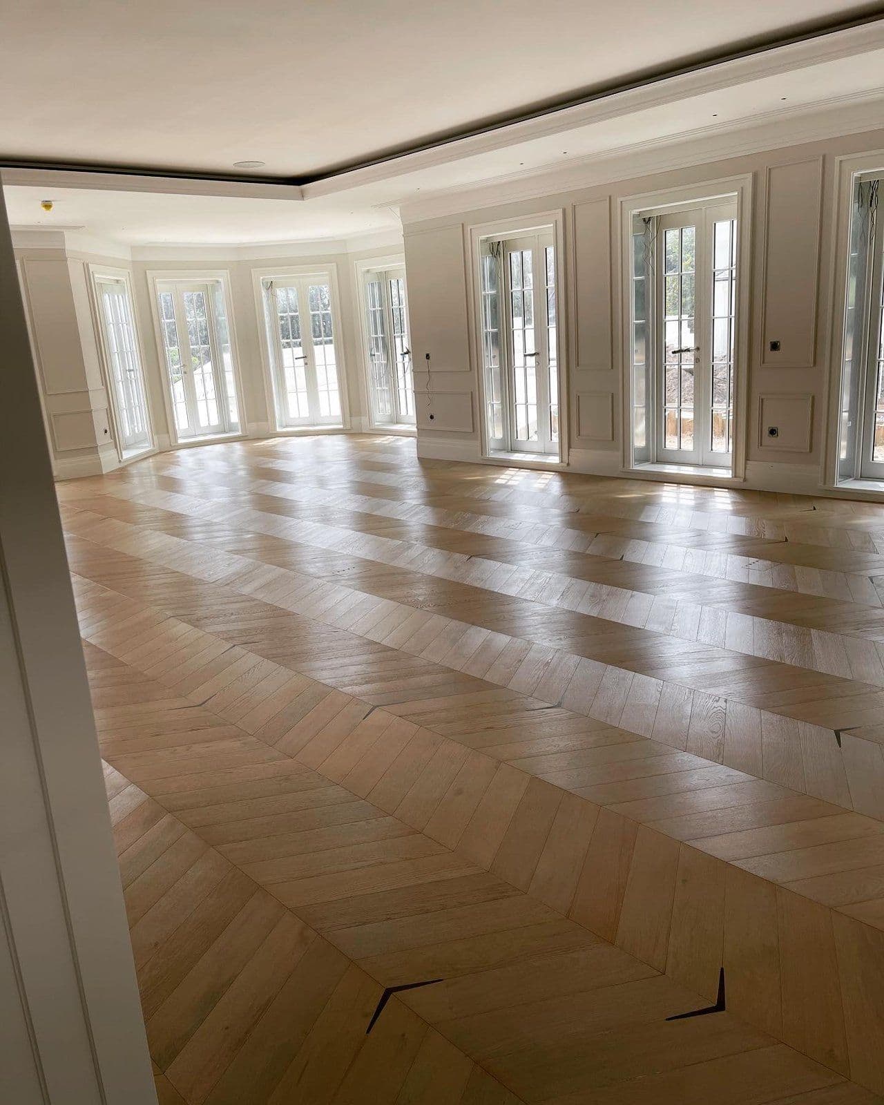 Chevron parquet flooring laid through a panelled room with French windows